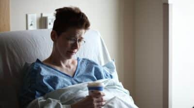 A female patient in a hospital bed looking forlorn.